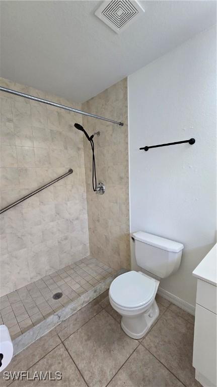 bathroom with toilet, tile patterned flooring, a tile shower, and vanity