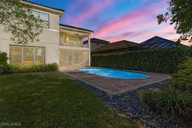 pool at dusk with ceiling fan, a patio area, and a lawn