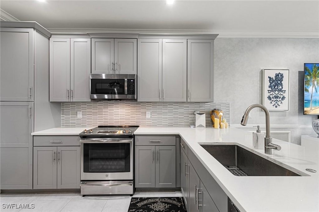 kitchen featuring stainless steel appliances, sink, backsplash, gray cabinets, and ornamental molding