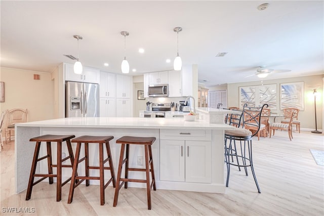 kitchen featuring decorative light fixtures, ceiling fan, a kitchen breakfast bar, stainless steel appliances, and white cabinets