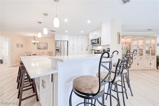 kitchen with a large island with sink, white cabinets, decorative light fixtures, stainless steel appliances, and a breakfast bar