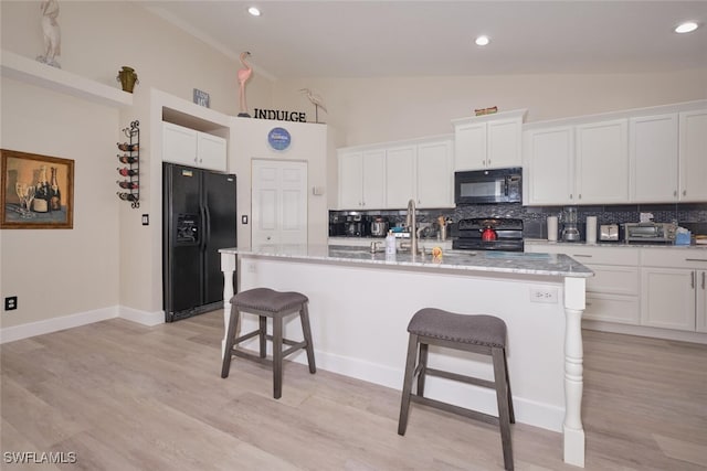 kitchen featuring black appliances, a kitchen island with sink, white cabinetry, and a kitchen bar