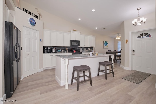 kitchen featuring white cabinetry, tasteful backsplash, a kitchen island with sink, hanging light fixtures, and black appliances