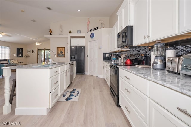 kitchen featuring vaulted ceiling, black appliances, light stone countertops, an island with sink, and white cabinets