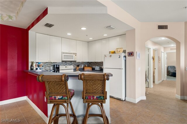 kitchen with white appliances, visible vents, arched walkways, white cabinets, and a peninsula