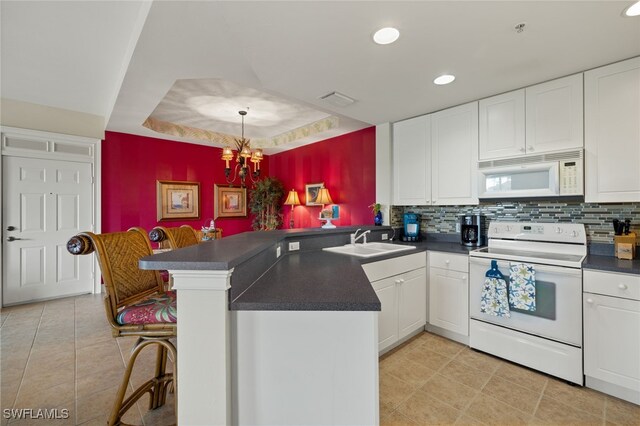 kitchen featuring dark countertops, an inviting chandelier, white cabinets, white appliances, and a peninsula