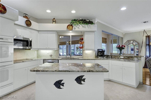 kitchen with white cabinets, appliances with stainless steel finishes, a center island, sink, and crown molding