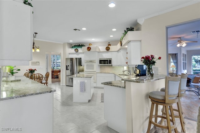 kitchen featuring kitchen peninsula, appliances with stainless steel finishes, ornamental molding, and white cabinetry