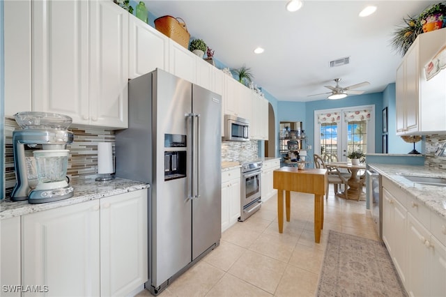 kitchen featuring light tile patterned floors, light stone counters, stainless steel appliances, white cabinetry, and a sink