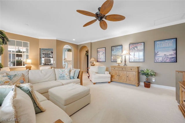 living room featuring arched walkways, light colored carpet, a ceiling fan, baseboards, and ornamental molding