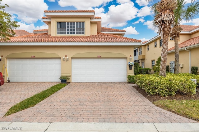 mediterranean / spanish home featuring a garage, a tiled roof, decorative driveway, and stucco siding