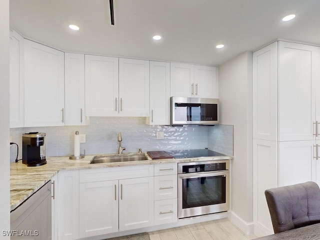 kitchen featuring backsplash, sink, light stone countertops, stainless steel appliances, and white cabinets