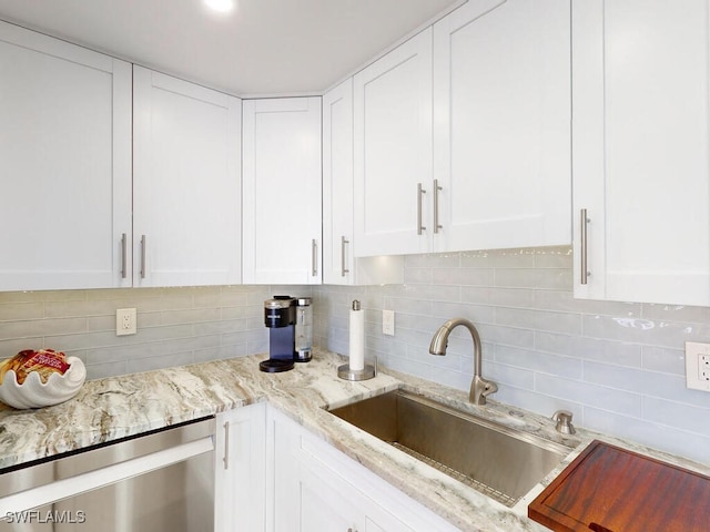 kitchen with tasteful backsplash, white cabinets, stainless steel dishwasher, light stone counters, and sink