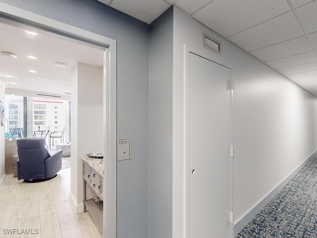 corridor with a drop ceiling and light hardwood / wood-style flooring