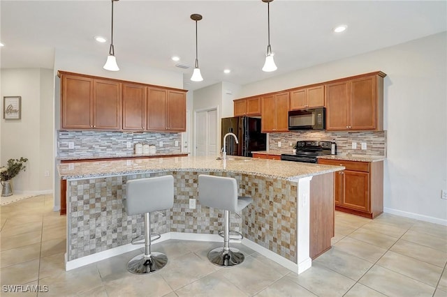 kitchen with light tile patterned floors, light stone countertops, black appliances, an island with sink, and a kitchen bar