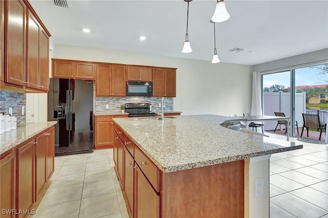 kitchen featuring black appliances, tasteful backsplash, hanging light fixtures, and an island with sink