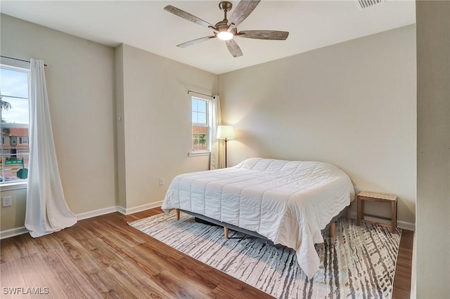 bedroom with ceiling fan, wood-type flooring, and multiple windows