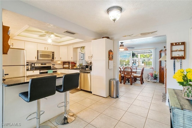 kitchen featuring a tray ceiling, crown molding, white cabinets, appliances with stainless steel finishes, and light tile patterned flooring