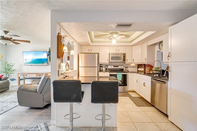 kitchen featuring a textured ceiling, stainless steel appliances, a kitchen bar, a tray ceiling, and white cabinets