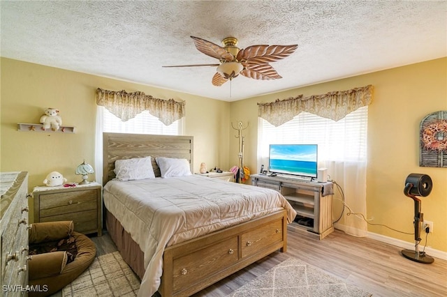 bedroom with a textured ceiling, ceiling fan, light hardwood / wood-style flooring, and multiple windows