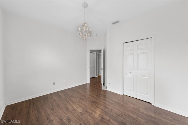 unfurnished bedroom with dark hardwood / wood-style floors, a closet, and a chandelier