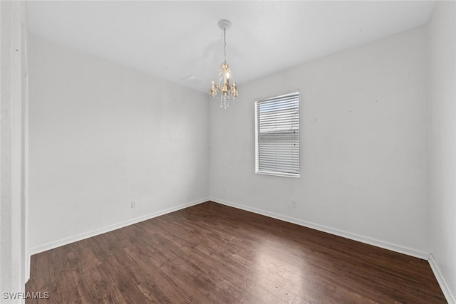 spare room with a chandelier and dark wood-type flooring