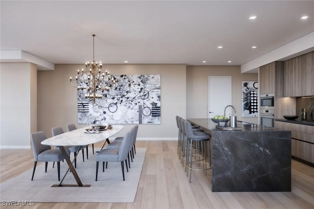 dining room with sink, light wood-type flooring, and a chandelier