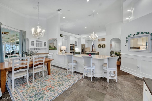 dining room with arched walkways, a notable chandelier, a decorative wall, ornamental molding, and wainscoting