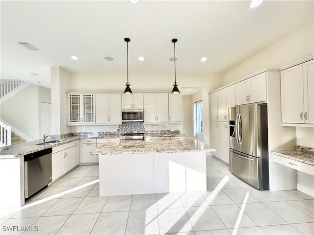 5161 Vizcaya St, Ave Maria, FL 34142 - kitchen featuring appliances with stainless steel finishes, a center island, a sink, glass insert cabinets, and light stone counters