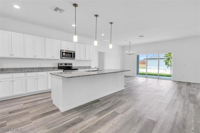 kitchen featuring stainless steel appliances, an island with sink, light stone countertops, white cabinets, and decorative light fixtures