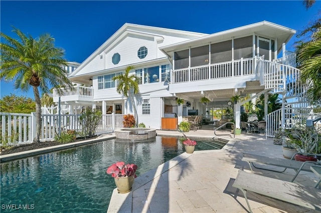 back of property with a sunroom, a swimming pool with hot tub, and a patio area