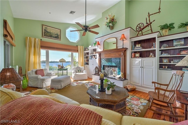 living room featuring high vaulted ceiling, a water view, light hardwood / wood-style flooring, ceiling fan, and a fireplace