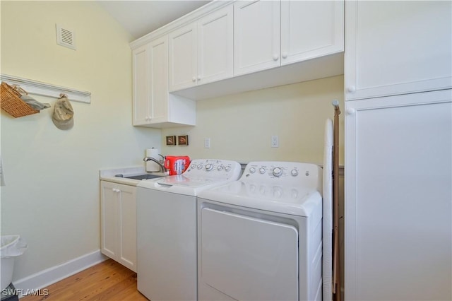 laundry area featuring washer and clothes dryer, cabinets, sink, and light hardwood / wood-style flooring