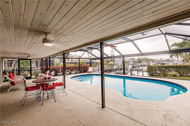 view of pool featuring ceiling fan, a patio, a water view, and glass enclosure