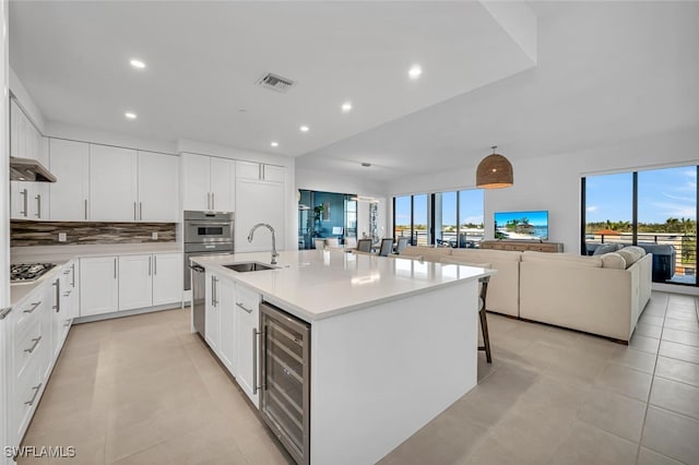 kitchen featuring sink, white cabinetry, a kitchen breakfast bar, an island with sink, and beverage cooler