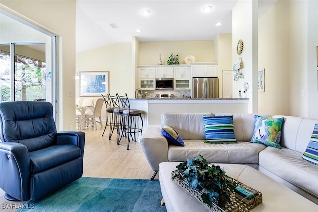 living room with sink, light hardwood / wood-style flooring, and lofted ceiling