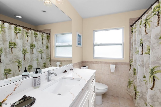 bathroom with toilet, tile patterned floors, tile walls, and a healthy amount of sunlight