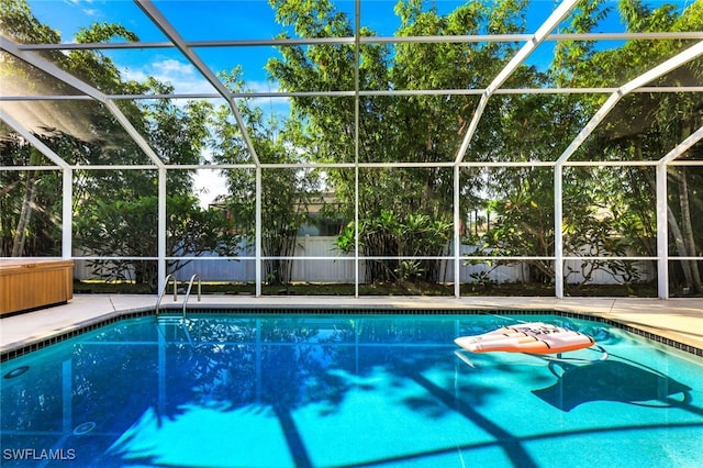 pool with a patio area, glass enclosure, and fence