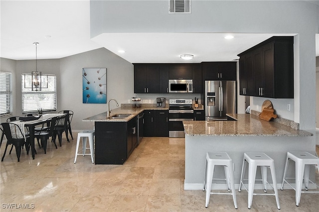 kitchen with a kitchen bar, kitchen peninsula, appliances with stainless steel finishes, pendant lighting, and sink