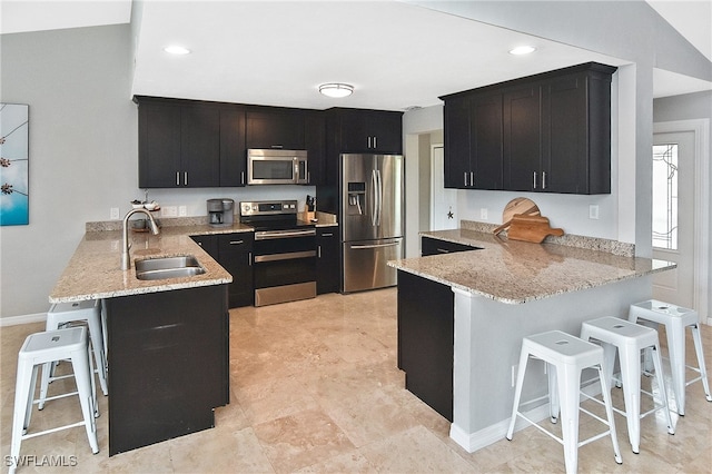 kitchen with light stone countertops, appliances with stainless steel finishes, sink, a kitchen breakfast bar, and kitchen peninsula