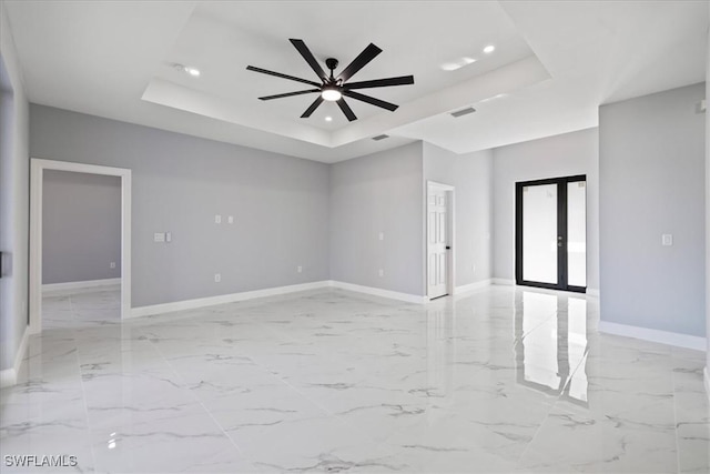 empty room featuring ceiling fan, a raised ceiling, and french doors