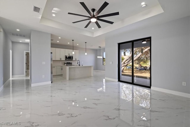 unfurnished living room featuring ceiling fan, a raised ceiling, and sink