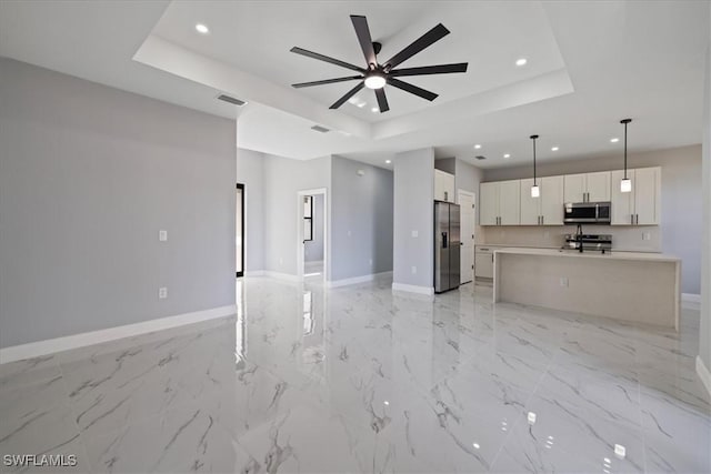 unfurnished living room with ceiling fan and a tray ceiling