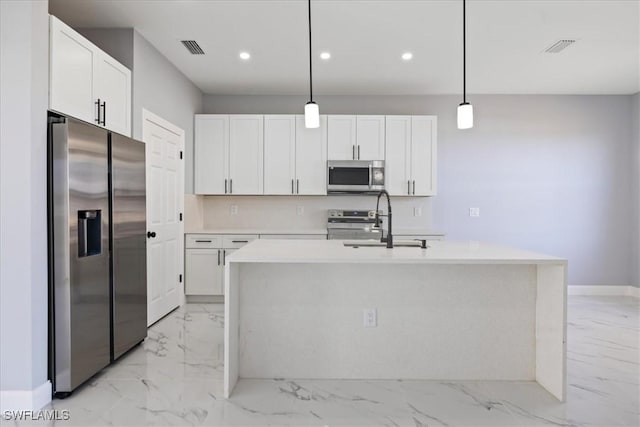 kitchen featuring white cabinets, stainless steel appliances, an island with sink, sink, and hanging light fixtures