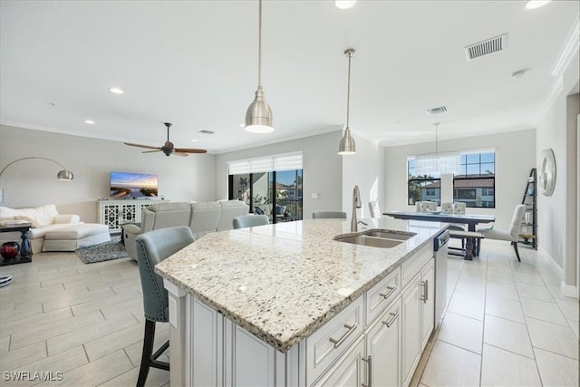 kitchen featuring sink, light stone counters, hanging light fixtures, a kitchen island with sink, and white cabinets