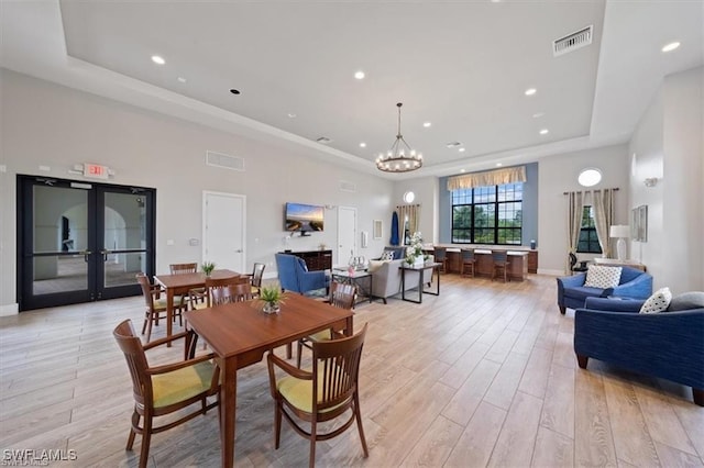 dining room with an inviting chandelier, french doors, a raised ceiling, and light wood-type flooring