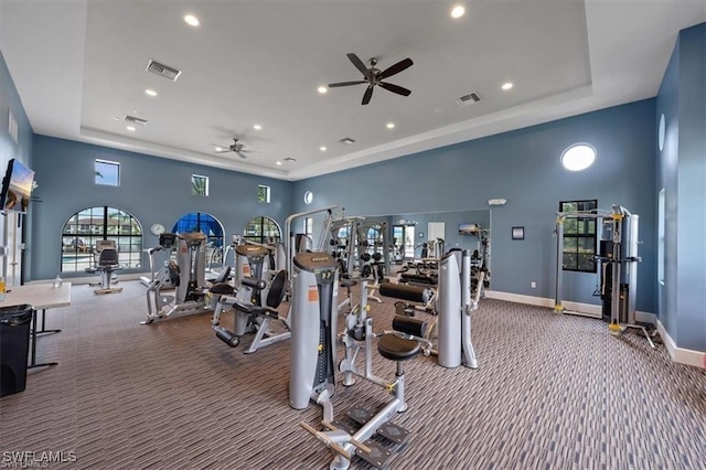 workout area featuring ceiling fan, carpet flooring, a tray ceiling, and a towering ceiling