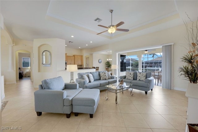 tiled living room featuring a tray ceiling, ornamental molding, and ceiling fan