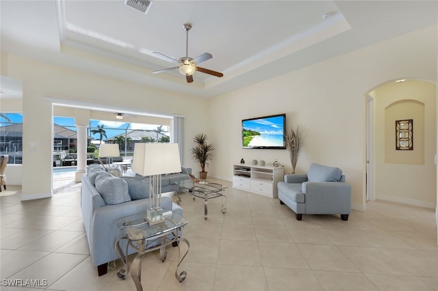 living room with a raised ceiling, crown molding, light tile patterned floors, and ceiling fan