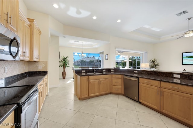 kitchen with a tray ceiling, pendant lighting, sink, kitchen peninsula, and stainless steel appliances